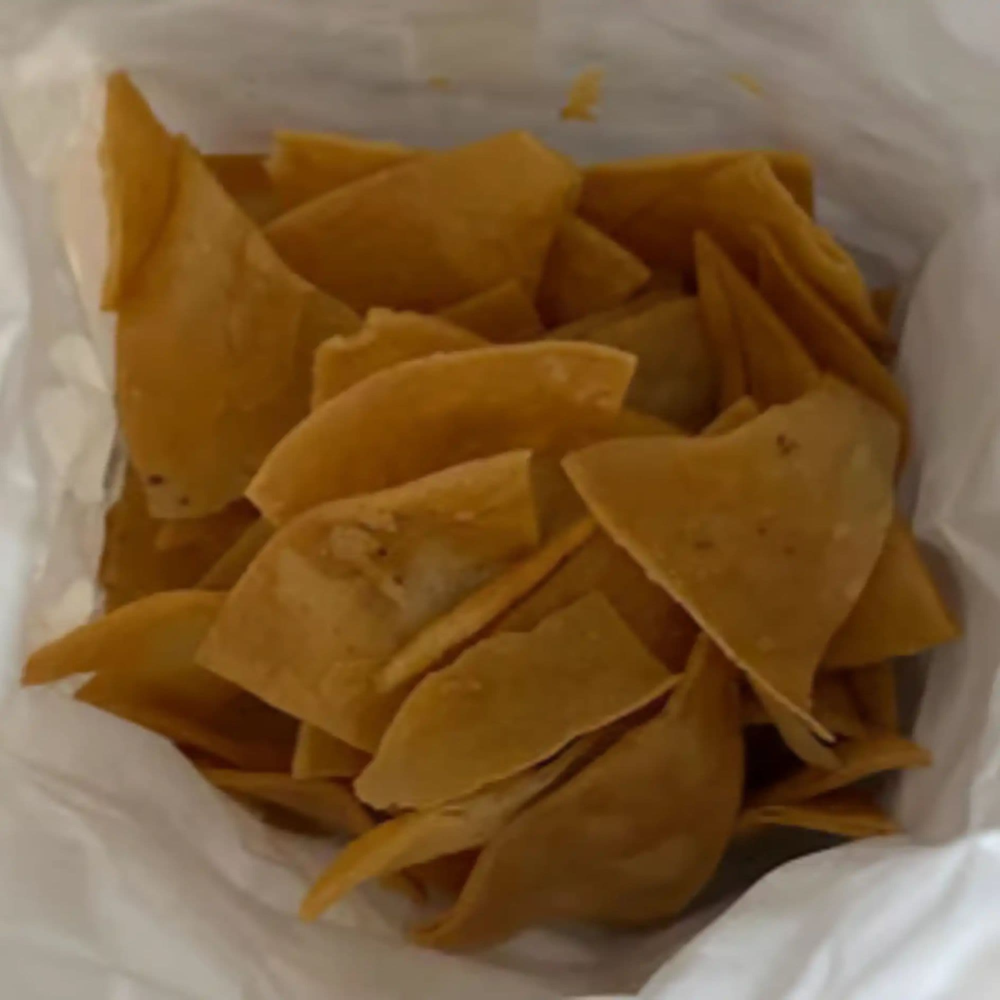Restaurant food photo before AI enhancement - Re-staged from informal paper bag takeout presentation to a professional white ceramic bowl. Bright, even lighting highlights the golden color and crisp texture of the chips, creating an appetizing restaurant-quality image.