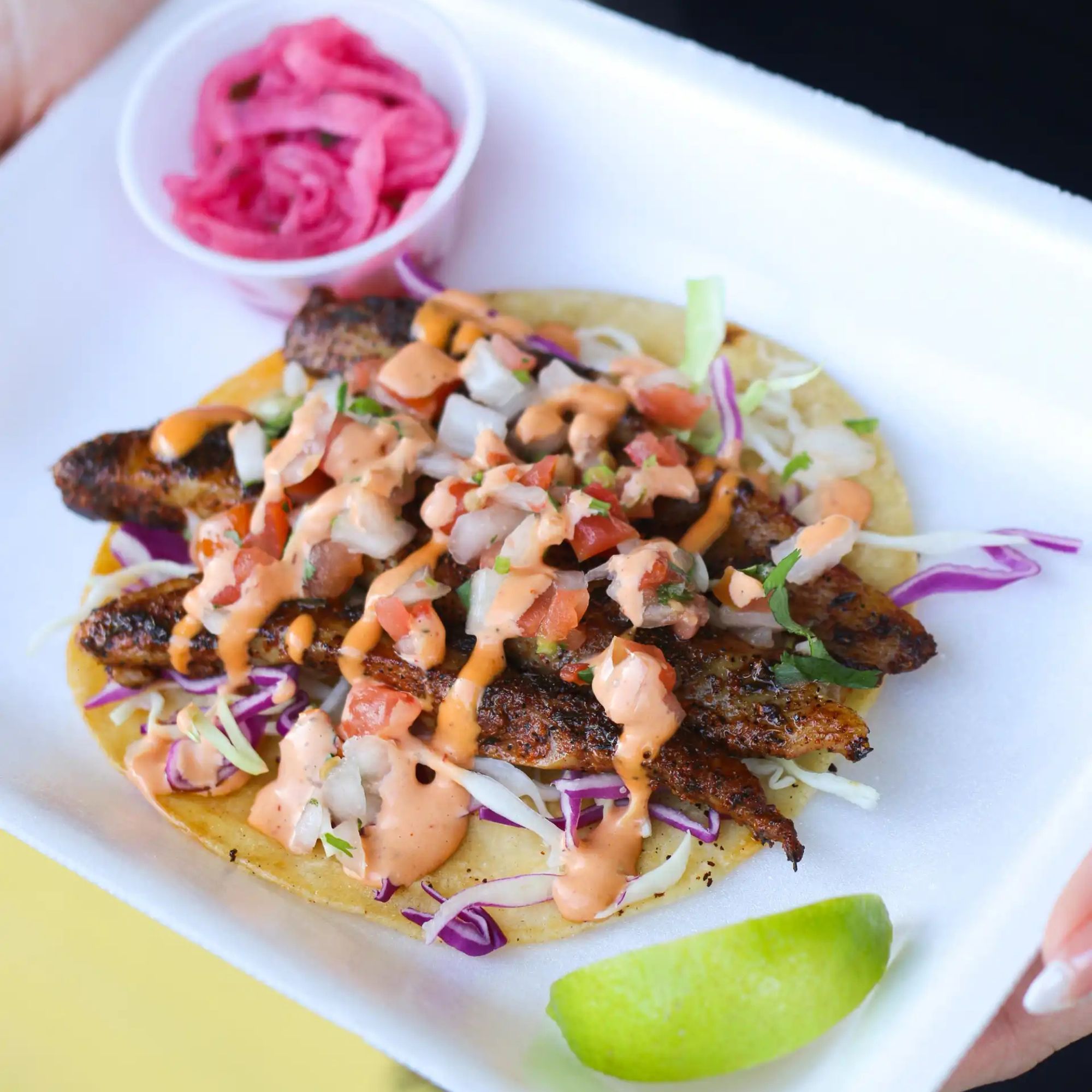 Restaurant food photo before AI enhancement - Transformed from a casual plate setting with yellow background to a clean white circular plate on pure white background. Enhanced lighting brings out vibrant colors in the ingredients, with improved saturation making the red onions and lime pop.